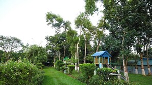 A lush garden with a play structure and a small blue-roofed building. - Swiss Valley Resort (Kamalganj)