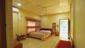A hotel room with a bed, a small table, a bench, a red carpet, and a door leading outside. - Swiss Valley Resort (Kamalganj)