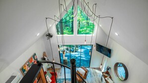 A modern interior with a staircase leading to a balcony overlooking a lush garden. - Romantic Cabin | Hot Tub, Soaking Tubs & Fire Pit (Bullard)