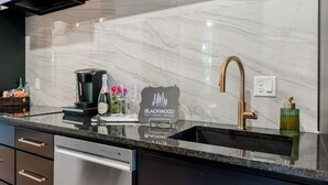 A modern kitchen with a marble backsplash, black cabinetry, and stainless steel appliances. - Romantic Cabin | Hot Tub, Soaking Tubs & Fire Pit (Bullard)