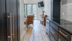 A modern kitchen with dark cabinetry, a large TV, and a dining area with a chair and table. - Romantic Cabin | Hot Tub, Soaking Tubs & Fire Pit (Bullard)