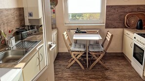 Una cucina compatta con una finestra, sedie in legno, un tavolino e elettrodomestici moderni.