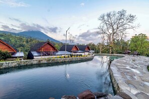 Eine ruhige Hotelsituation mit mehreren Holzhütten, einem mit Steinplatten ausgelegten Pool und üppiger Vegetation.