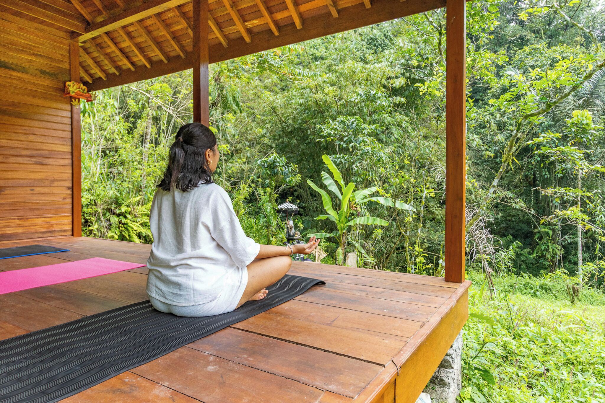 Una persona meditando en una cubierta de madera con vista a la vegetación densa.