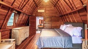 Een slaapkamer met een houten plafond, een bed met een gestreept dekbed, een dressoir en een hanglamp.