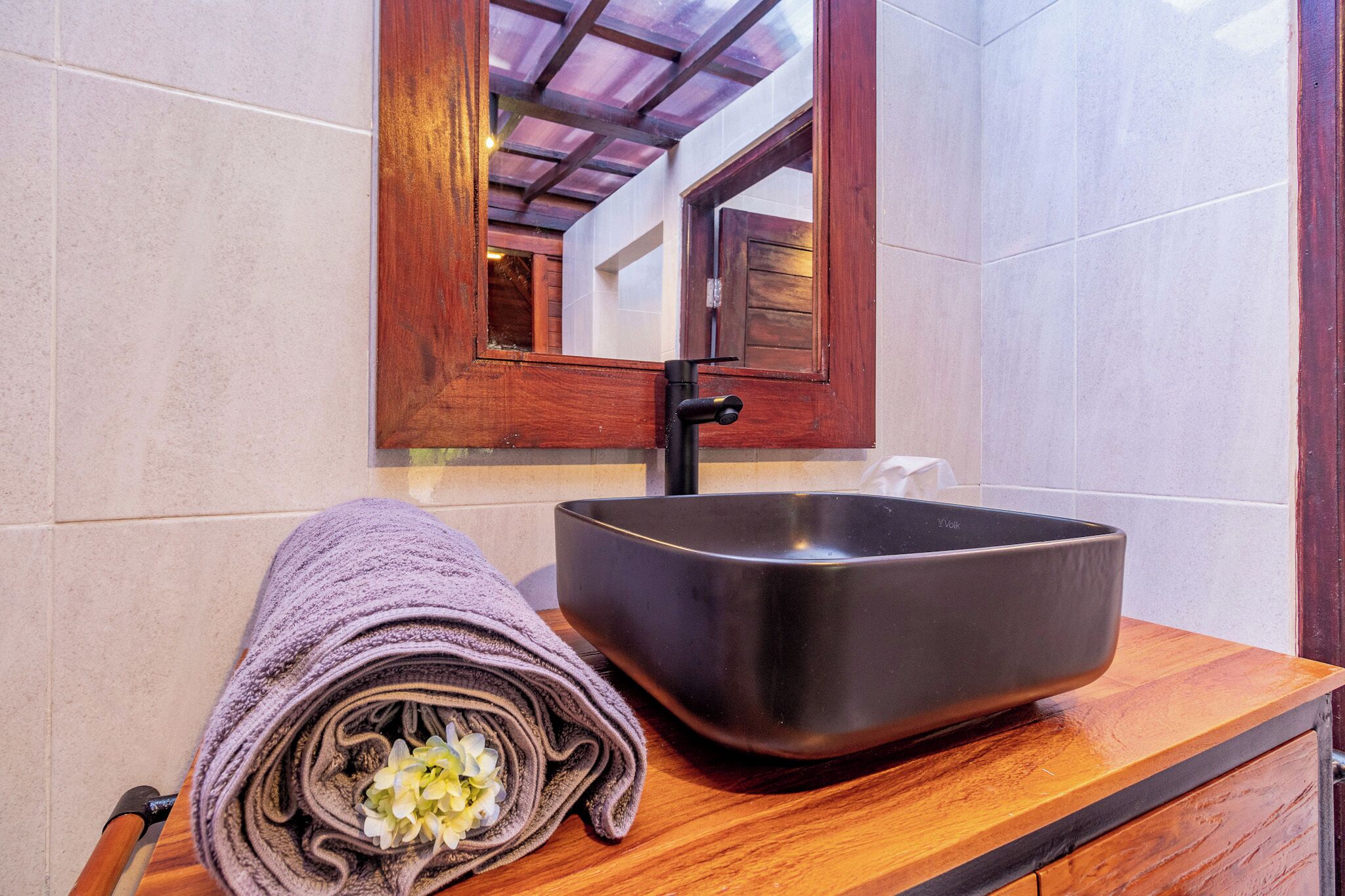 Un baño con tocador de madera, lavamanos tipo cuenco negro y espejo sobre él.