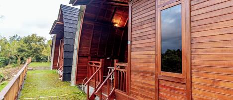 A wooden cabin with a porch, a staircase, and a view of the surrounding greenery.