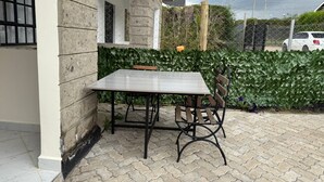 A patio with a table and chairs, a stone wall, and a hedge.