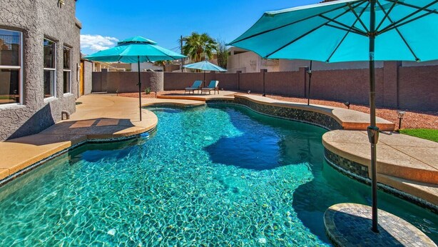 Une piscine aux eaux cristallines, bordée de carreaux, entourée d’un patio aménagé avec des chaises longues et des parasols.