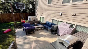 Un patio trasero con mobiliario exterior, una parrilla y un aro de baloncesto.