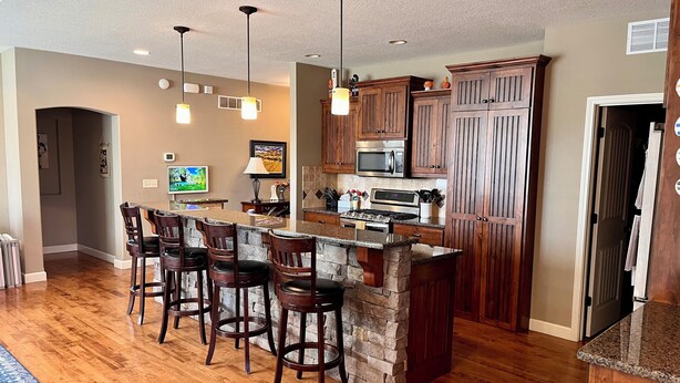 Una cocina con una isla central, taburetes de bar, armarios de madera y un microondas.