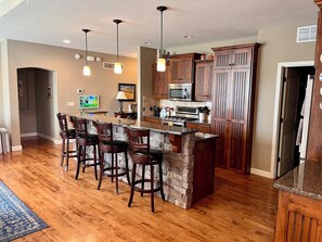 Una cocina con una isla central, taburetes de bar, armarios de madera y un microondas.