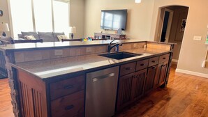 Una cocina con una isla central, armarios de madera, lavavajillas y un ventanal amplio.