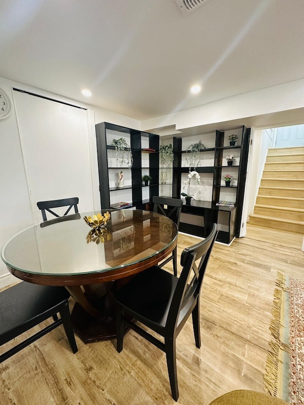 A dining area with a round glass table, black chairs, and a black bookshelf with plants.