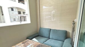 Un espace de vie moderne avec une table en verre, un canapé bleu et une vue sur un immeuble doté de nombreuses fenêtres.