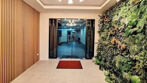 Un hall d'entrée moderne avec un mur composé de lambris en bois, un jardin vertical verdoyant et un tapis rouge menant à un couloir.