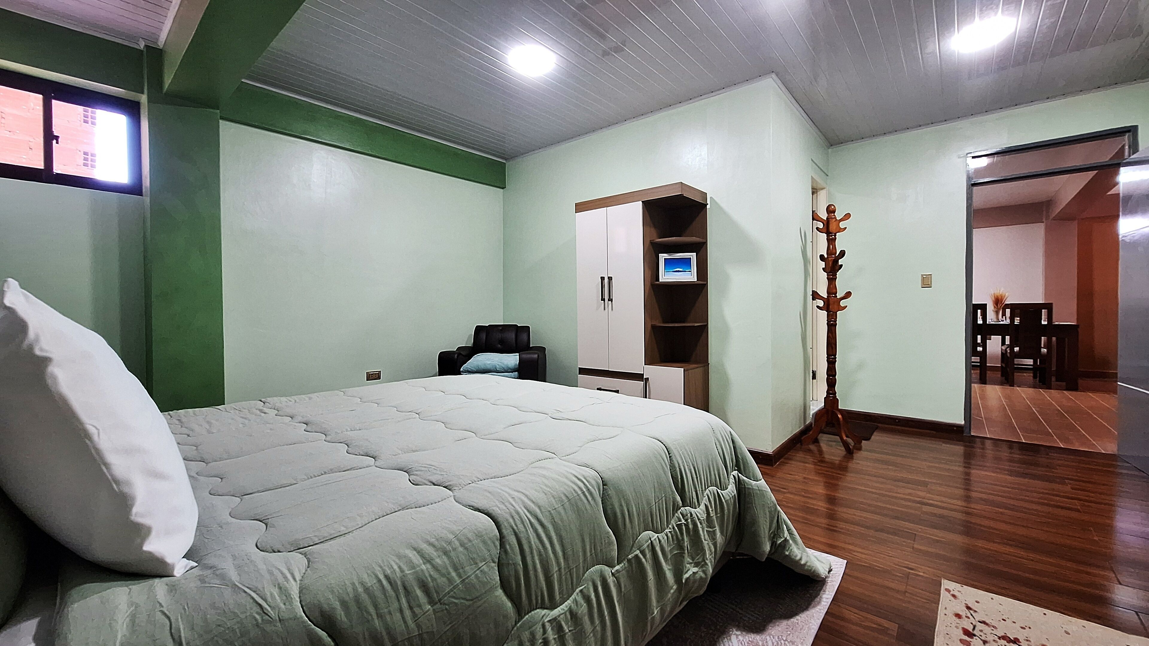 A bedroom with a bed, a TV, a wardrobe, and a coat stand.