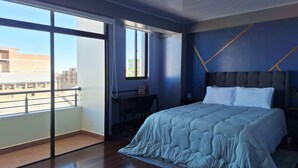A modern bedroom with a large bed, a desk, and a view of the city through a sliding door. - Enjoyable 2-bedroom, 2-bathroom apartment with heating and Wi-Fi in Uyuni (Uyuni)