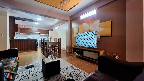 A modern living room with a TV, a dining area, and a kitchen in the background. - Enjoyable 2-bedroom, 2-bathroom apartment with heating and Wi-Fi in Uyuni (Uyuni)