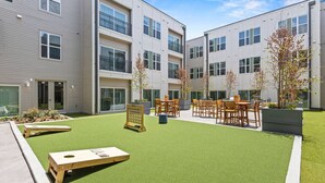 A courtyard with artificial grass, outdoor seating, and a small wooden table. - Trendy Bishop Arts | Game Room + Gym + Yoga (Dallas)