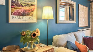 A room with a blue wall, a framed map, a lamp, a sofa, and a vase with sunflowers. - 2 bedroom accommodation in Tideswell (Tideswell)