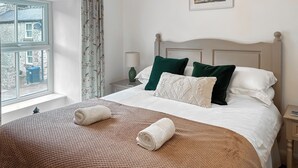 A neatly made bed with a brown blanket and two rolled towels, a nightstand with a lamp, and a window with curtains. - 2 bedroom accommodation in Tideswell (Tideswell)