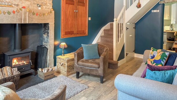 A cozy living room with a stone fireplace, a wooden chest, a comfortable armchair, and a staircase leading to an upper level. - 2 bedroom accommodation in Tideswell (Tideswell)