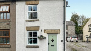 A two-story building with a green door, a window with a hanging basket, and a parked car in the driveway. - 2 bedroom accommodation in Tideswell (Tideswell)