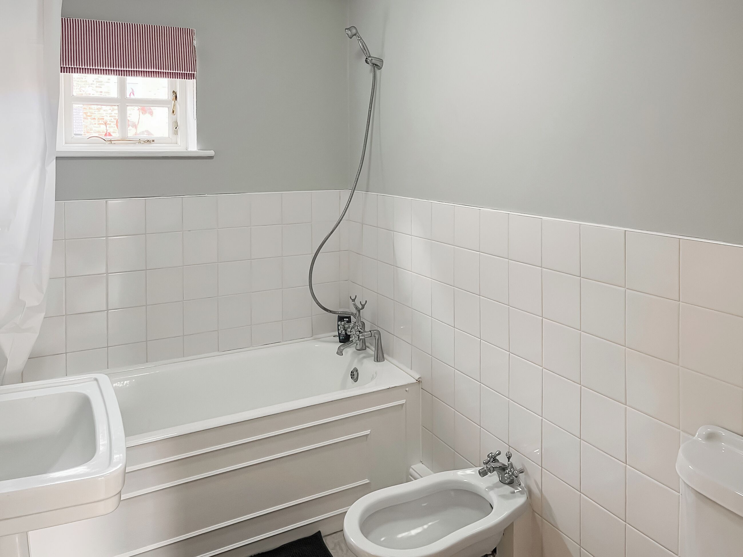 Un baño con bañera, un bidé y una ventana con un adorno a rayas.