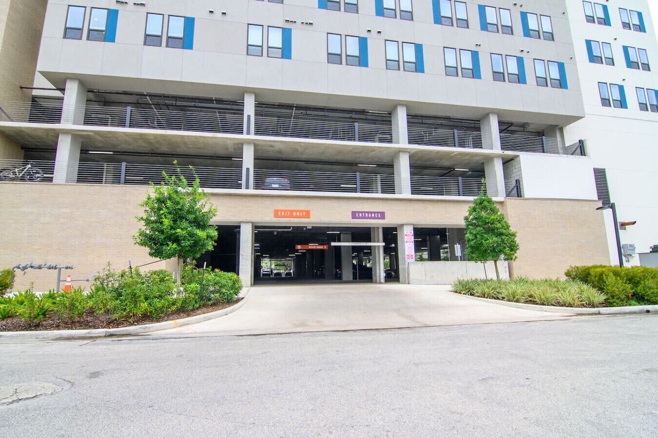 A modern building with an entrance and exit sign, a covered parking area, and a landscaped entrance.
