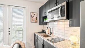 A modern kitchen with dark cabinets, a stainless steel microwave, a granite countertop, and a window with blinds.