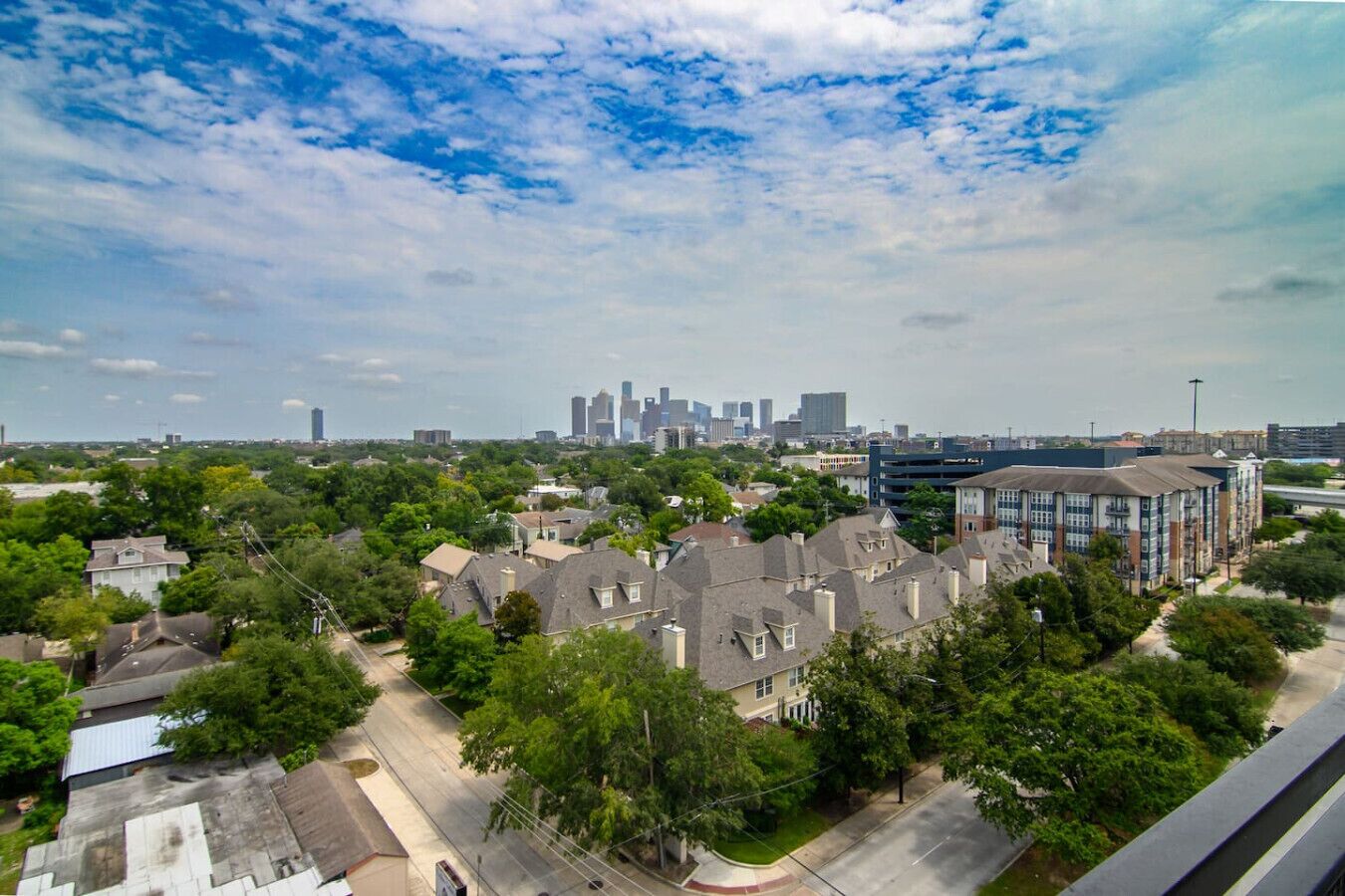 Un quartier résidentiel où se côtoient des maisons unifamiliales et des immeubles d’appartements, le tout entouré de verdure et offrant une vue lointaine sur les gratte-ciel de la ville.