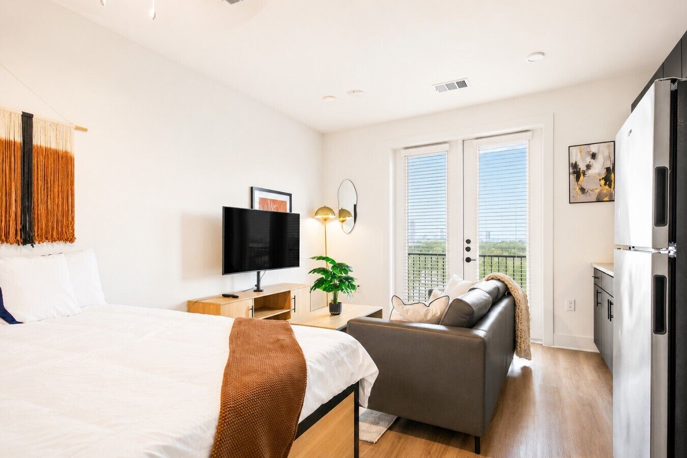 A modern bedroom with a bed, a TV, a sofa, and a balcony with a view.