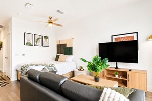 Ein modernes Schlafzimmer mit einem Bett, einem Deckenventilator, einem Fernseher und einer Pflanze.