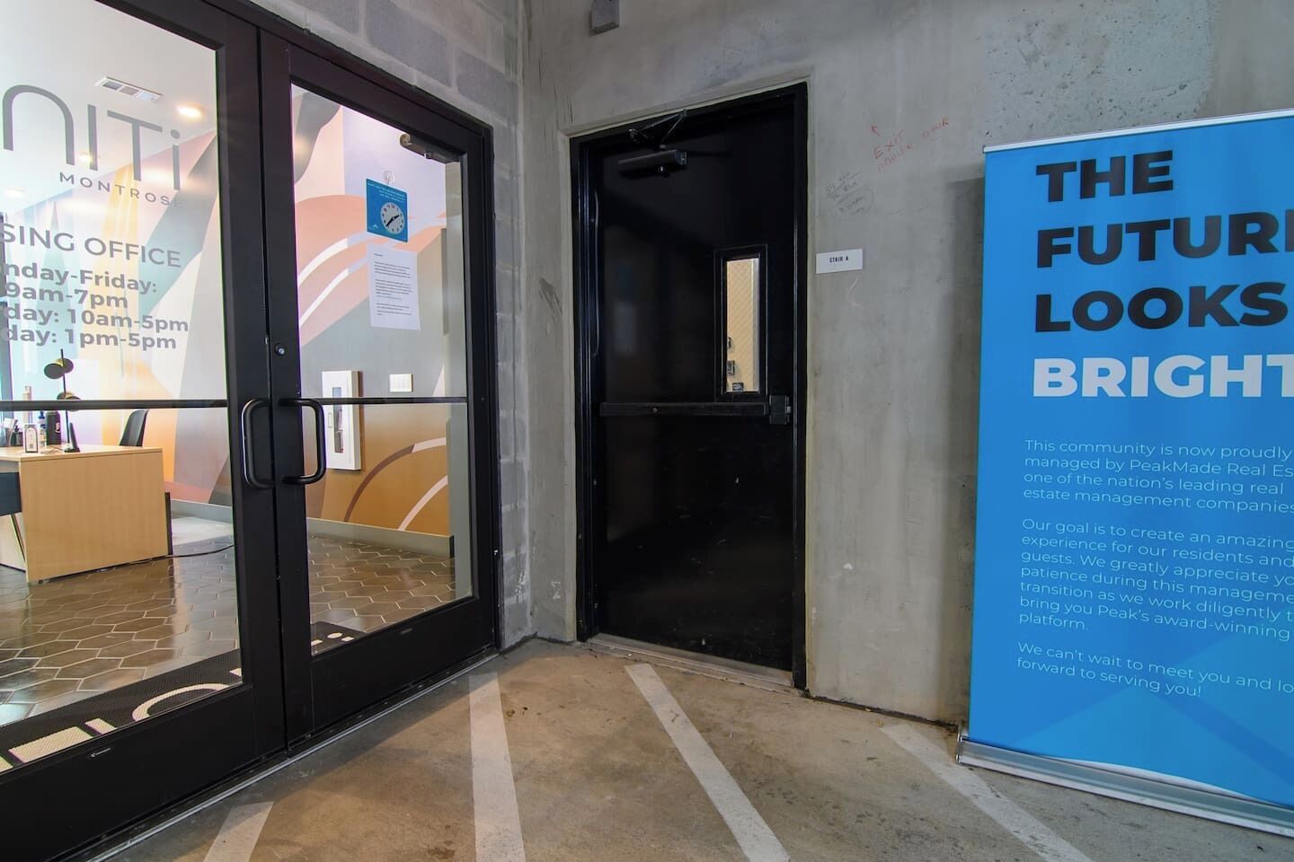 Entrada de hotel com porta de vidro, balcão de recepção e um cartaz anunciando o futuro.
