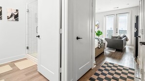 A modern apartment with a hallway leading to a living area, a visible door, and a checkered rug.
