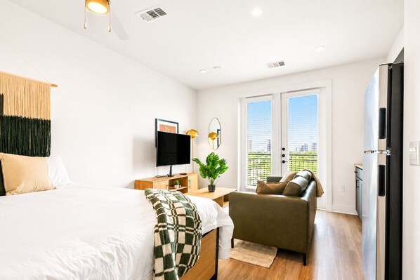 Ein modernes Schlafzimmer mit Bett, Fernseher, Sofa und Balkon mit Blick.