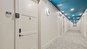 A hotel hallway with white doors, numbered room signs, and a blue ceiling.