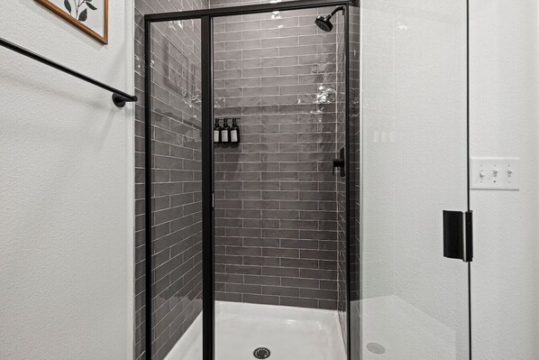 A modern bathroom with a glass shower enclosure, a white bathtub, and a tiled wall.