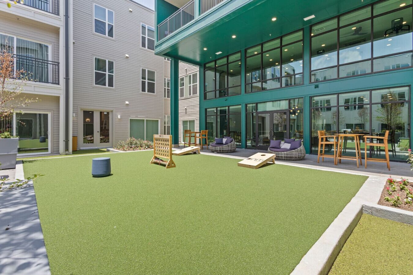 A courtyard with artificial turf, seating areas, and a building with large windows and a green facade.