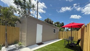 A small, single-story house with a front door, a patio with a red umbrella, and a wooden fence. - Bienes House private property in Brandon (Brandon)
