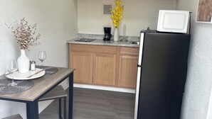 A compact kitchen with wooden cabinets, a black refrigerator, a coffee maker, and a vase with flowers on the counter. - Bienes House private property in Brandon (Brandon)
