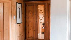 A wooden interior with a framed picture on the wall, a wooden door with a diamond-shaped window, and a white wall.
