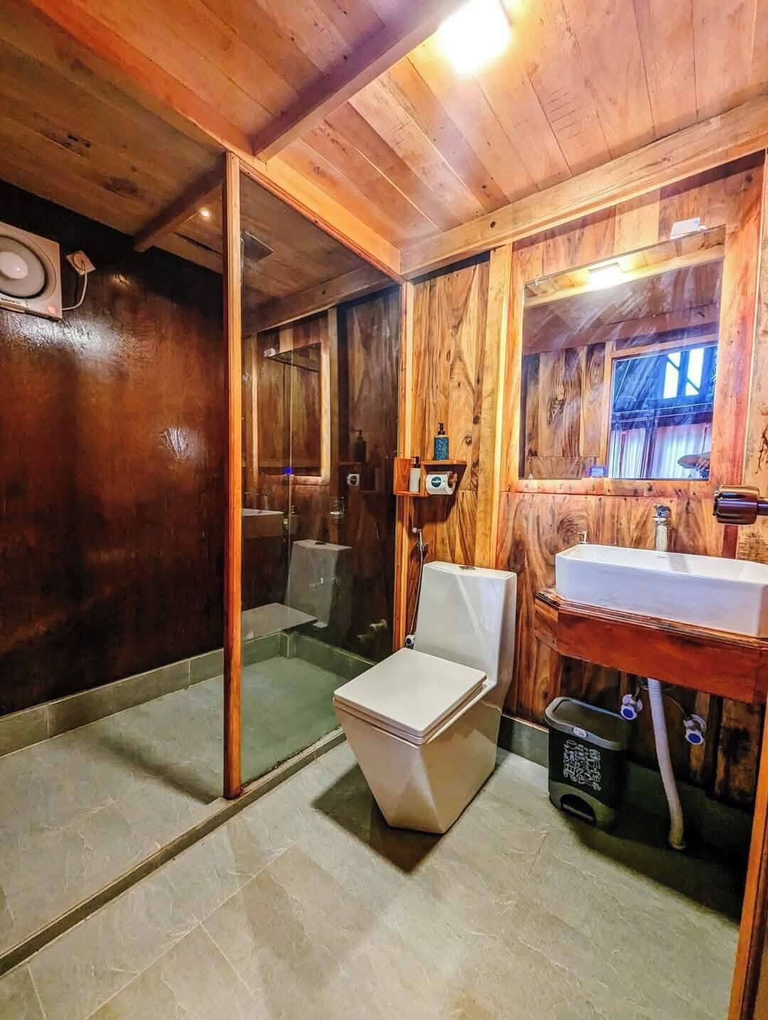 A wooden cabin bathroom with a toilet, sink, and shower.