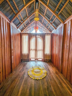 A room with wooden walls and a sloped ceiling, featuring a central circular rug and a hanging light fixture. - JungleBari Mangrove Resort (Dacope)