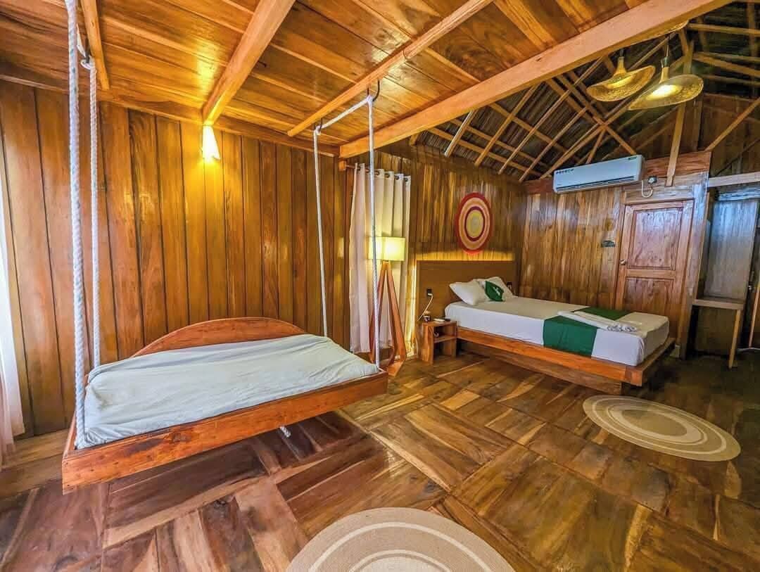 A wooden room with two beds, a hanging light, and a ceiling fan.