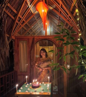 A woman in a traditional sari standing in a wooden hut with a thatched roof, decorated with string lights and candles. - JungleBari Mangrove Resort (Dacope)
