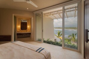 Une chambre avec un lit, une salle de bain avec un miroir et une porte-fenêtre coulissante donnant sur un balcon avec vue sur la mer.
