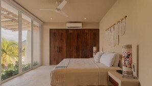Quarto com cama, ventoinha no teto, guarda-roupa espaçoso e vista para palmeiras.