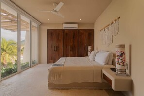 Ein Schlafzimmer mit einem Bett, einem Deckenventilator, einem großen Kleiderschrank und Blick auf Palmen.